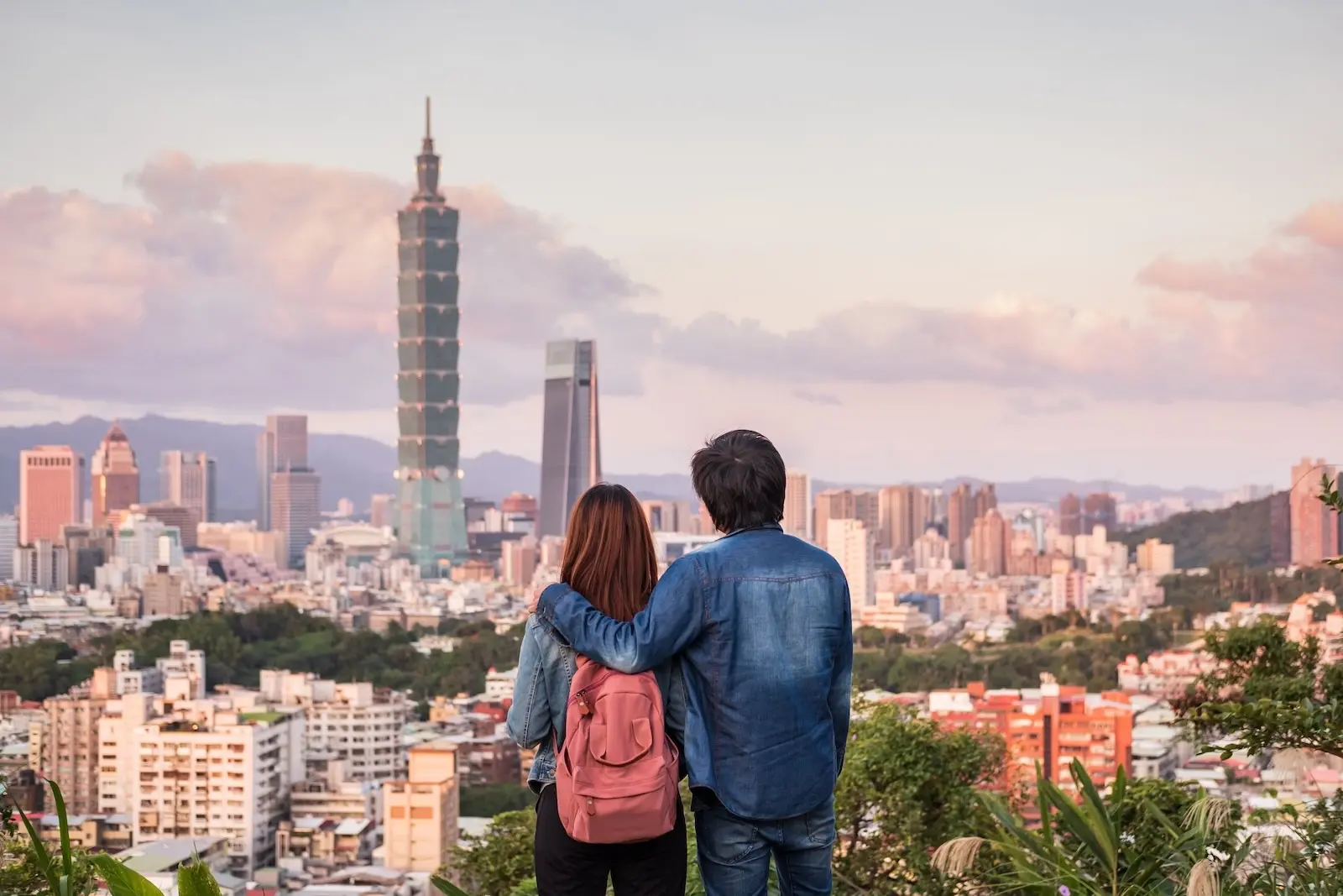 Couple admiring the Taipei 101 skyline from a hilltop overlook at sunset